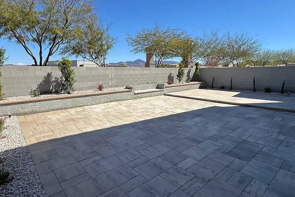 A spacious paver patio with a backdrop of native desert plants and trees, designed for low maintenance landscaping. The scene showcases a modern Las Vegas landscaping project with clear blue skies and mountains in the distance.| Sun Valley Landscape Las Vegas