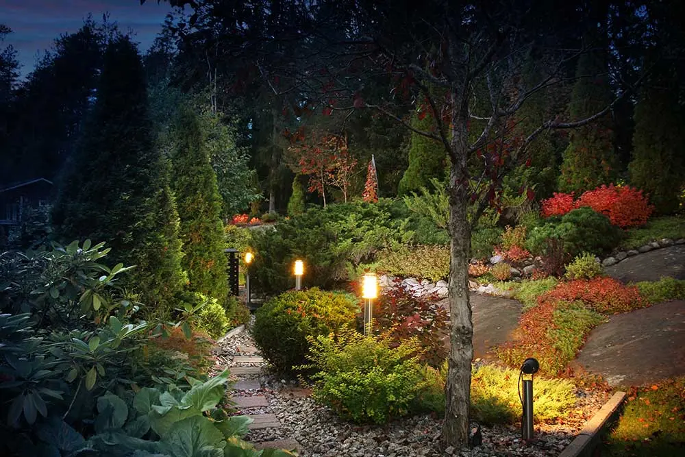 A beautifully lit garden path with lush greenery and vibrant flowers showcases expert landscape design, ideal for Las Vegas landscaping. The scene features a serene ambiance with strategically placed lighting enhancing the nighttime view.| Sun Valley Landscape Las Vegas