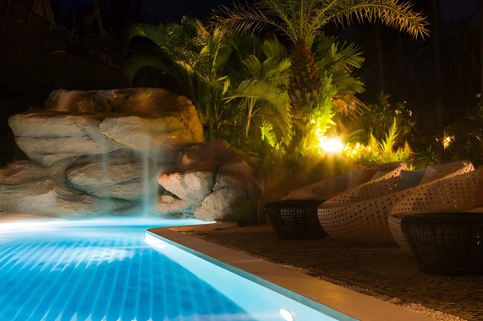 Fall Landscape Lighting Ideas That Add Safety and Style to Your Las Vegas Home1 Poolside landscape lighting with palm trees and waterfall feature glowing under warm lights.